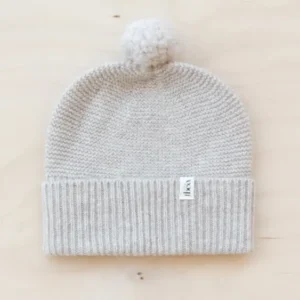 TBCo Merino Wool Baby Beanie in oatmeal melange with white pom-pom, knitted ribbed hem and small brand label