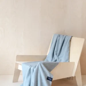 TBCo Lambswool Small Blanket in Light Grey Melange draped elegantly over wooden lounge chair showing texture and fringe detail