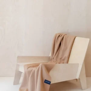 TBCo Lambswool Small Blanket in Camel draped elegantly over a light wooden chair, showcasing its soft texture and fringed edges