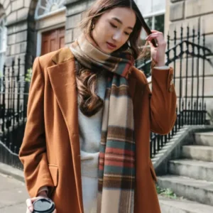 A person wearing TBCo's Stewart Dress Antique Tartan Lambswool Oversized Scarf styled with brown coat on Edinburgh street steps