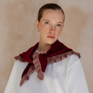 Young woman wearing TBCo Merino Wool Triangle Scarf in Burgundy Ruffle, featuring playful rose trim, draped over white T-shirt, showcasing elegant silver hoop earrings.