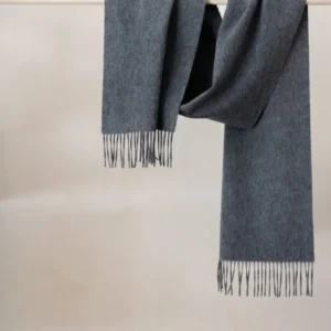 Luxurious TBCo charcoal melange cashmere scarf with black fringe detail, draped elegantly over wooden rail against neutral wall